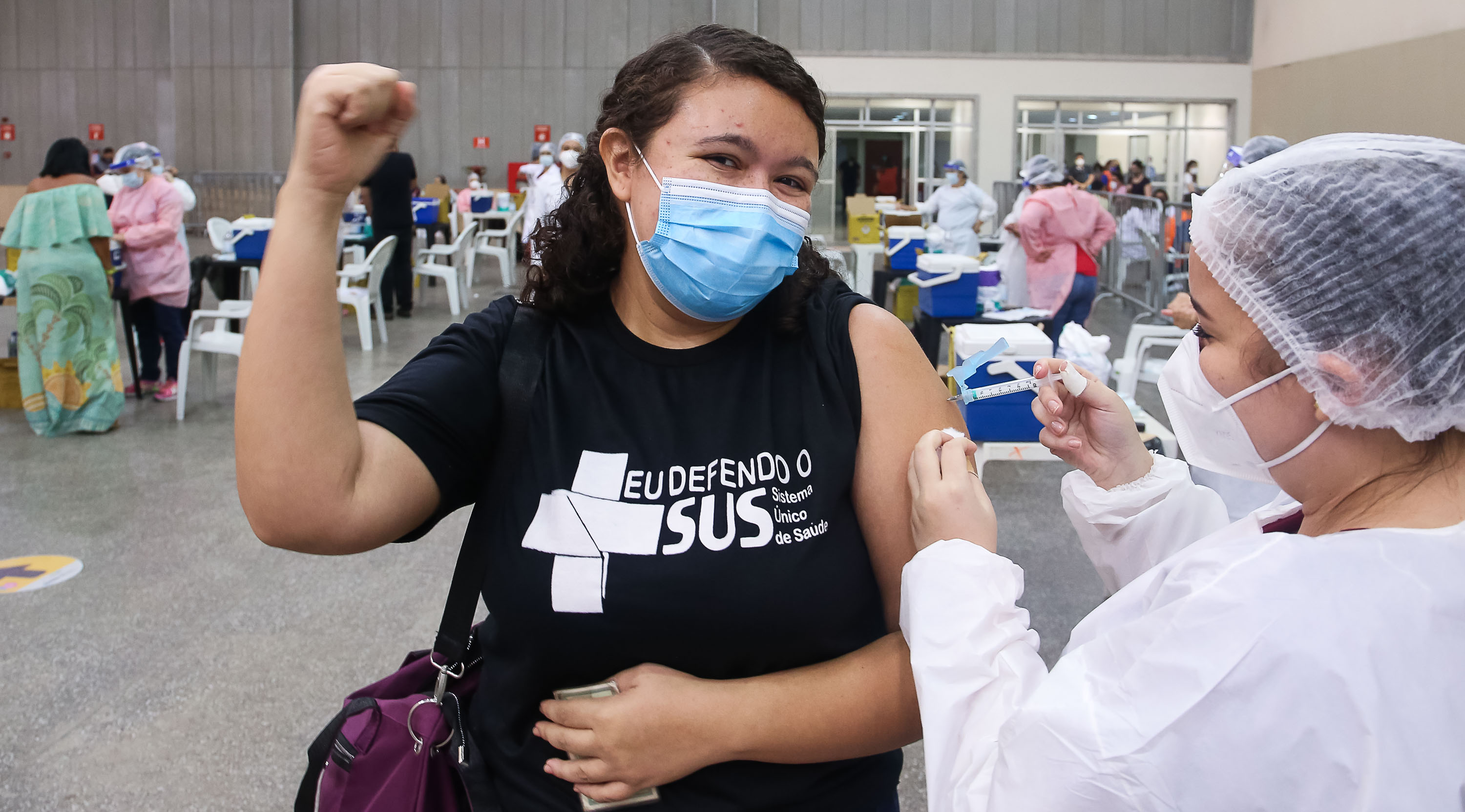 mulher com a camisa do SUS e máscara é vacinada